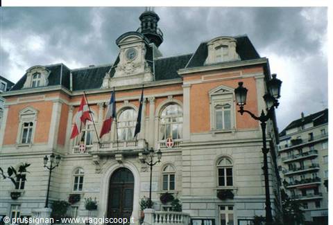 Aix-les-Bains town hall, ochre facade with clock and French flags under cloudy sky