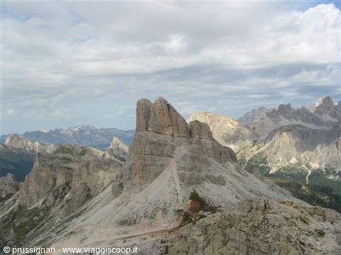 Dolomite rock spire under clouds, scree slopes and grey walls around