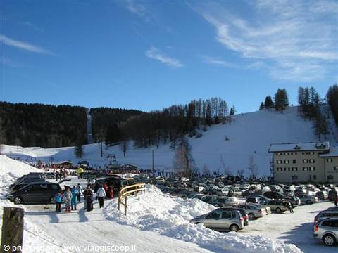 Parking lot full of cars near snowy ski slopes with skiers carrying equipment