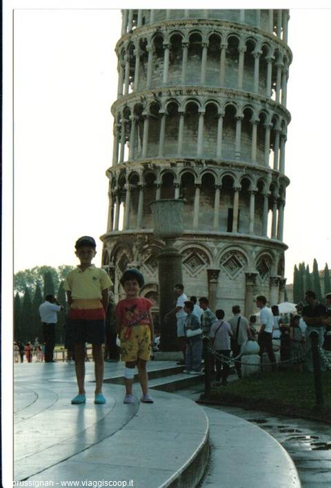 Two children standing in front of the Leaning Tower of Pisa, white marble and tourists