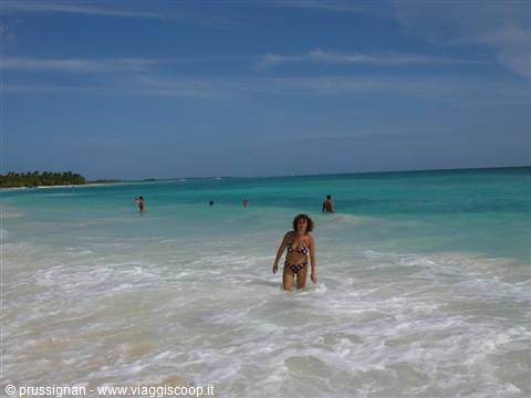 Woman in swimsuit wading through foam, turquoise water and white sand beach