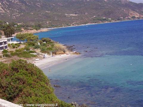 White sandy beach between Mediterranean shrubs and turquoise sea, hills behind