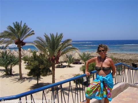 Woman in bikini and sarong on terrace with palms and tropical beach