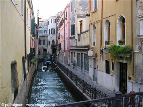 Narrow canal between colorful facades in Venice, moored boat beneath the bridge