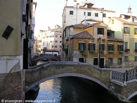 Stone bridge over green canal in Venice, colorful houses and bell tower