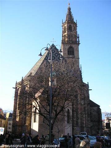 Bolzano Cathedral with stone bell tower and tiled roof under blue sky