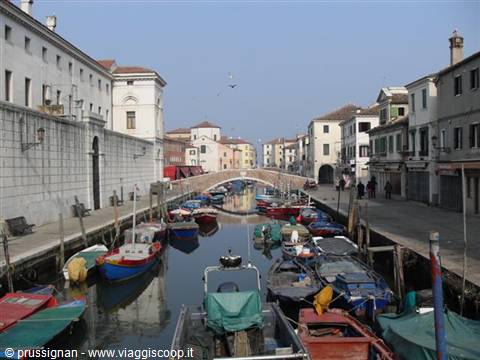 Chioggia canal with moored colorful fishing boats and brick bridge