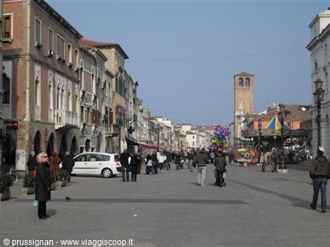 Pedestrians along Corso del Popolo in Chioggia, with bell tower and colorful stalls