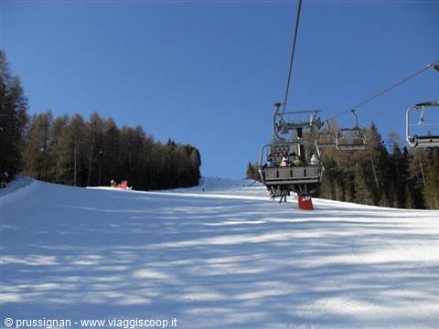 Chairlift with skiers above a snowy ski slope between firs, blue sky