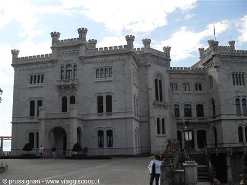 Tourists in front of Miramare Castle, white crenellated facade under cloudy sky