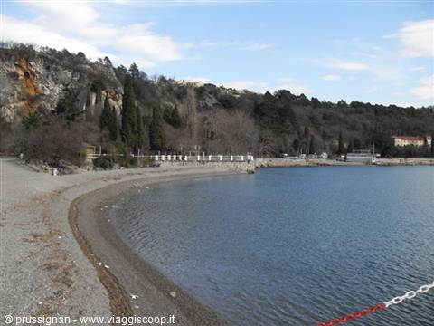 Gravel beach beneath rocky cliffs and pines, calm sea in Trieste