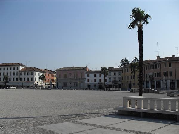 Cobblestone square with palm tree and colorful buildings under blue sky