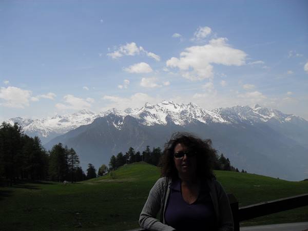 Woman with sunglasses on green meadow, snowy Alps behind