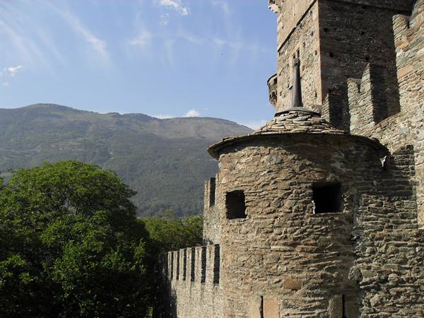 Round stone tower with battlements of the castle, green trees and mountains