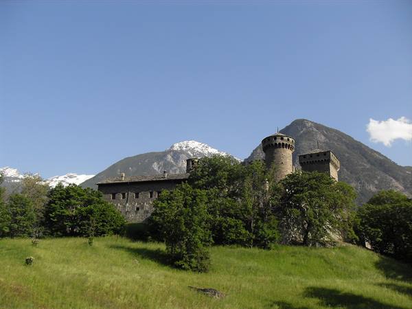 Fénis stone castle with crenellated towers among trees and snowy peaks