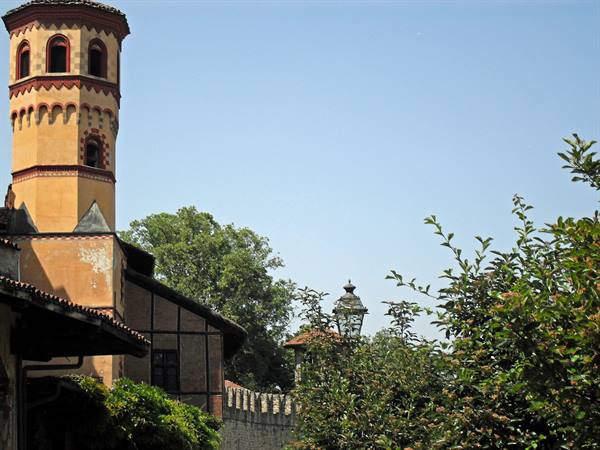 Brick and terracotta tower of Turin's Borgo Medievale among green trees