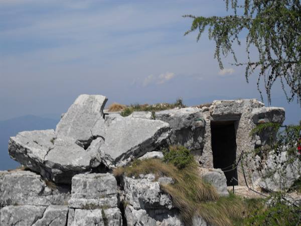 Bunker carved into limestone rock in the mountains, dark entrance among boulders and grass