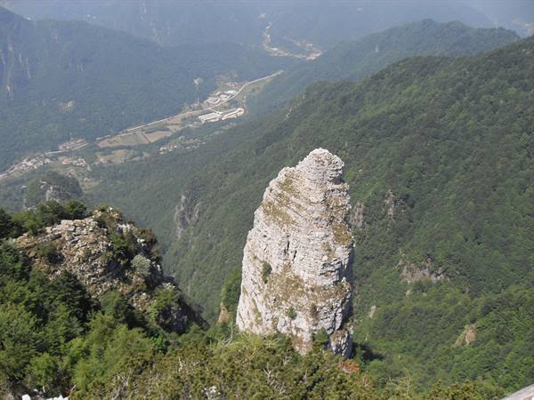 Limestone rock pinnacle rising above green forests, valley with roads and buildings below