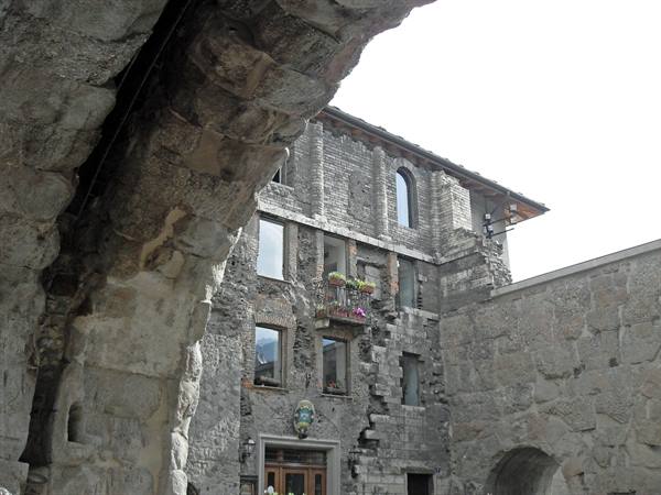 Ancient stone arch beside medieval building with windows and flowers
