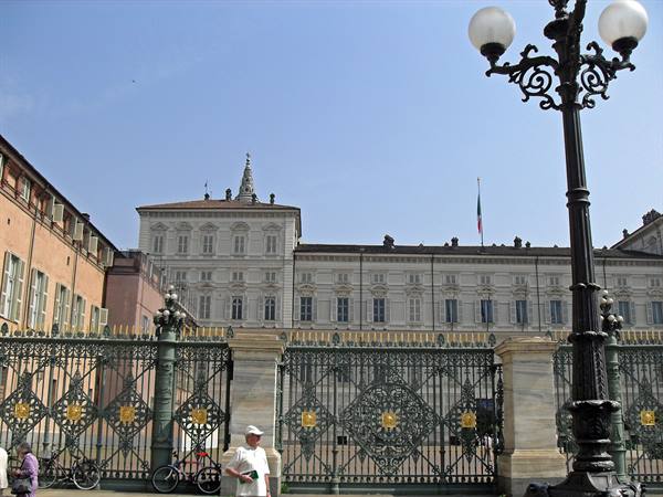 Wrought-iron gate in front of Turin's Royal Palace, ornate lamppost and pedestrians