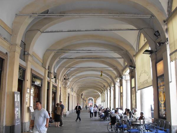 Arcaded portico with outdoor café, people walking beneath the vaults