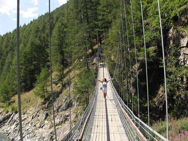 Woman in white skirt arms outstretched on wooden suspension bridge