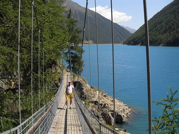 Tourist on wooden suspension bridge over turquoise Lake Vernagt between mountains