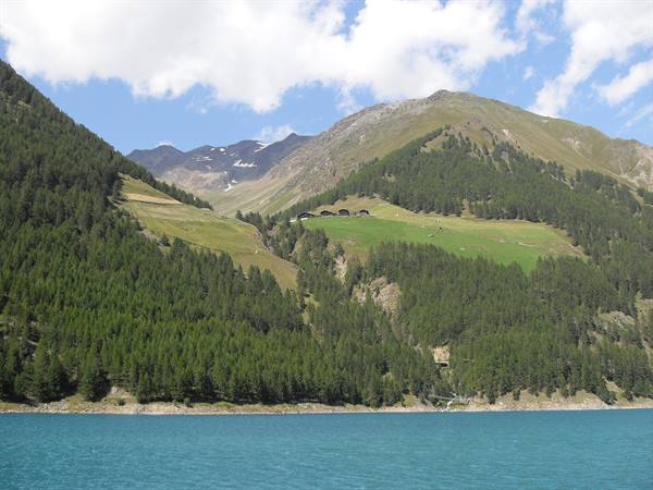 Turquoise lake beneath forested mountains and wooden alpine huts