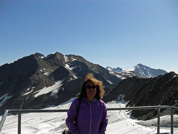 Woman in purple jacket in front of snowy rocky mountains, clear blue sky