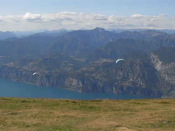 Paragliders soaring above Lake Garda from a high grassy slope