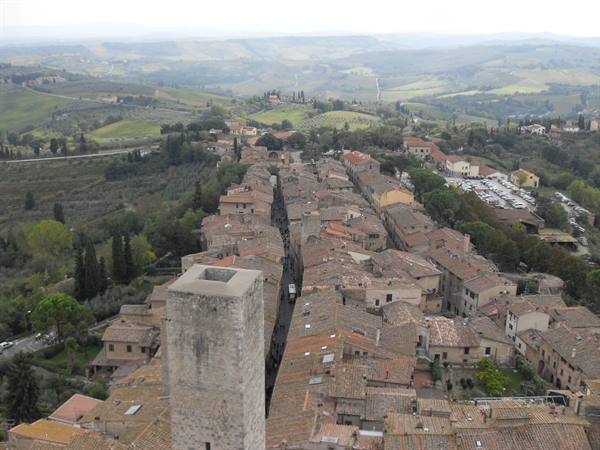 Stone medieval tower above San Gimignano rooftops, Tuscan hills under grey light