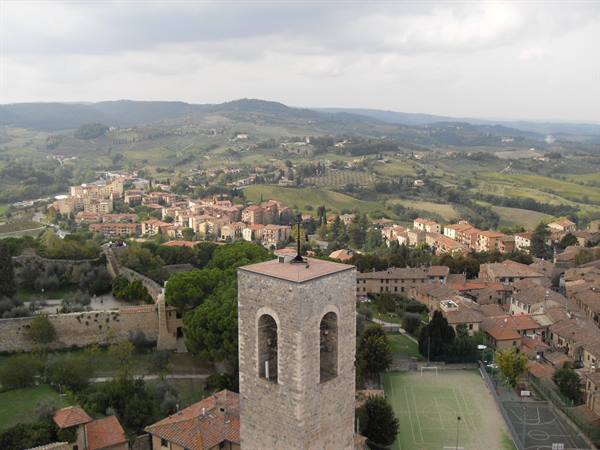 Stone bell tower rising above rooftops and hills of San Gimignano