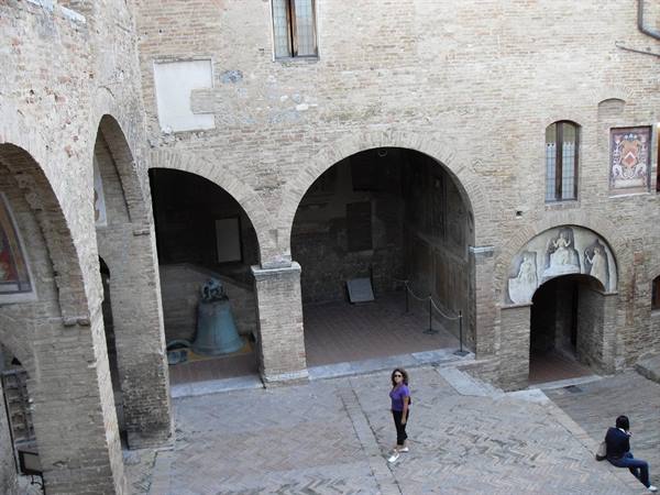 Woman walks in brick cloister with arches and medieval bell