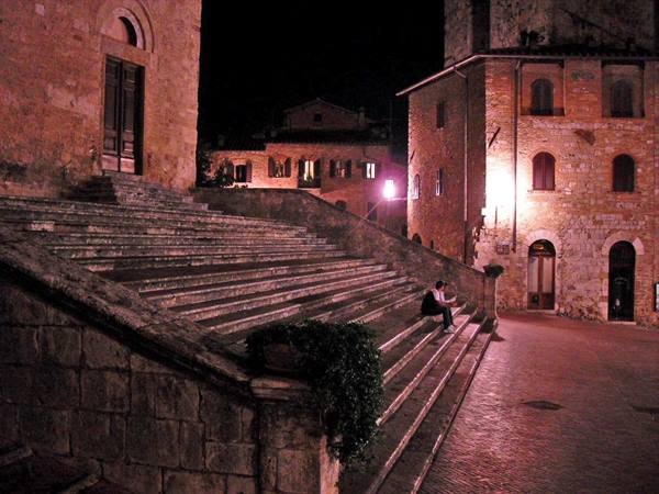 Person sitting on stone steps of Piazza del Duomo in San Gimignano at night