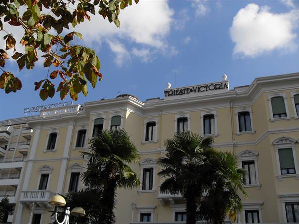 Yellow Hotel Trieste Victoria building with palms and leaves in foreground