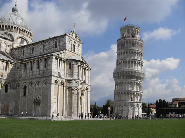 Tourists on green Piazza dei Miracoli with Pisa cathedral and leaning tower
