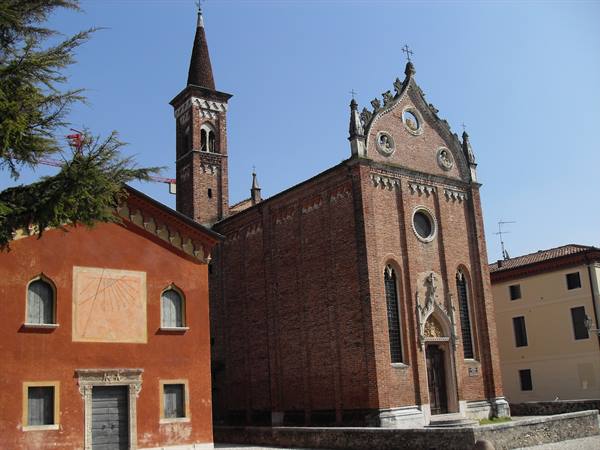 Gothic brick church with bell tower and rose window beside ochre houses