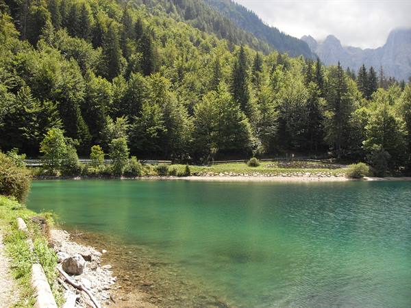 Emerald green lake with stony shore, conifer forest and cloudy mountains