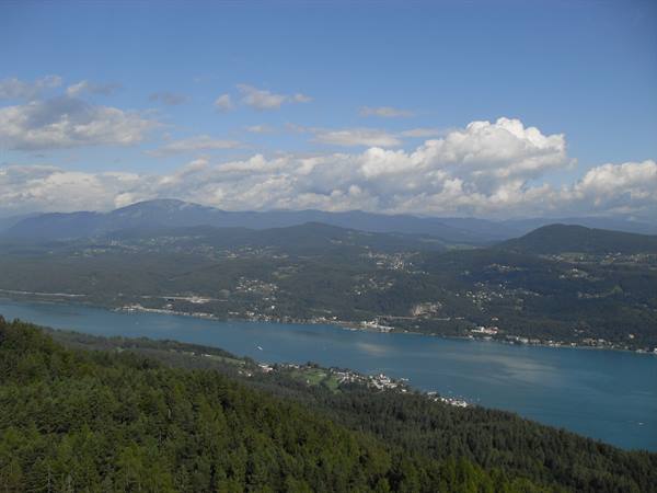 Turquoise Wörthersee lake among forests and hills, white clouds in the sky