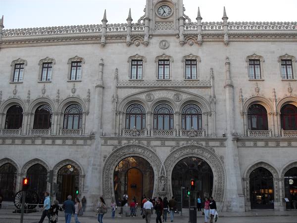 Tourists walk in front of the stone facade of Rossio railway station in Lisbon