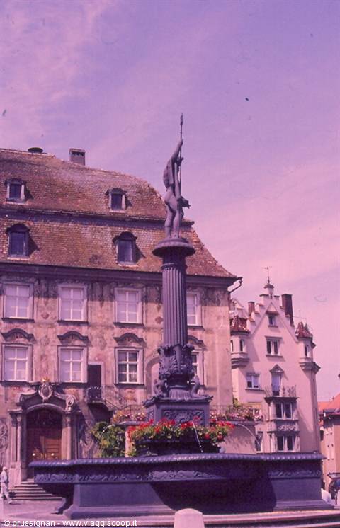 Cast-iron fountain with Neptune statue in front of painted buildings