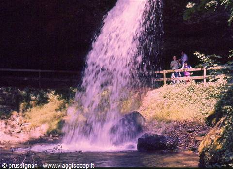Tourists behind a wooden fence watching a waterfall plunge into the pool