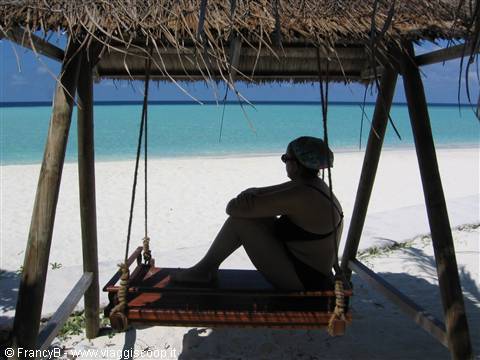 Woman in black swimsuit sitting on wooden swing with thatched roof on beach