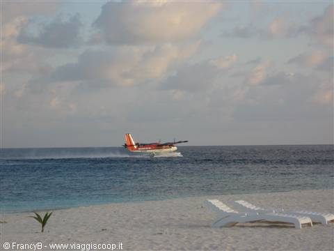 Red and white seaplane taking off from turquoise sea, white beach with loungers