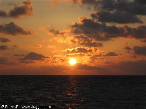 Low sun behind dark clouds reflects on the choppy sea