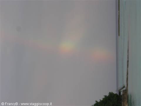 Faint rainbow in the gray sky next to a building wall