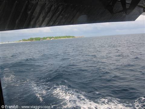 Tropical palm island seen from the boat, white wake on blue ocean