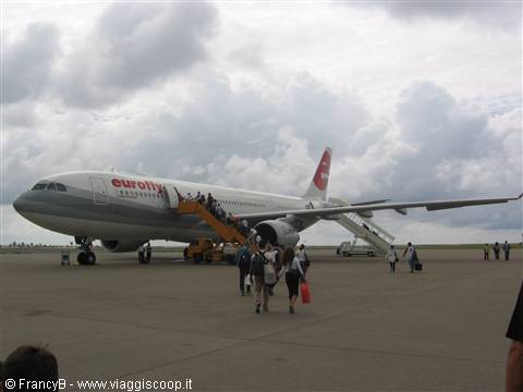 Passengers board the Eurofly plane via mobile stairs under cloudy sky