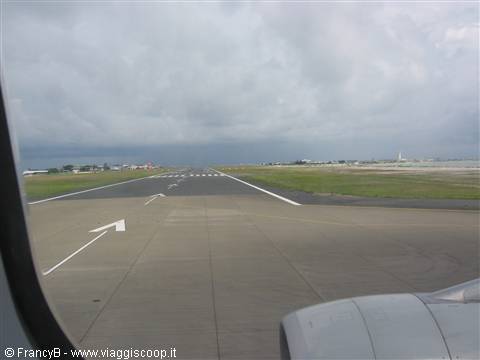 Runway with white arrows seen from airplane window under cloudy sky