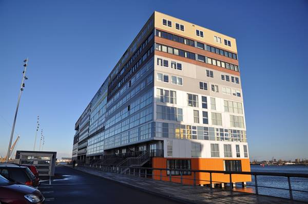 Colorful modern building by the water, parked cars under blue sky